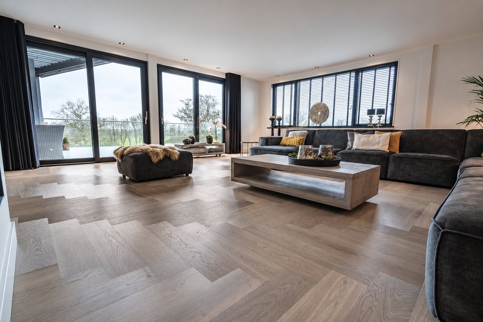 Salon avec parquet bâton rompu en chêne grisé, canapés gris et grandes baies vitrées